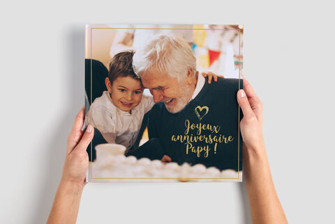 Deux personnes regardent affectueusement un album photo décoré de "Joyeux anniversaire Papy!".