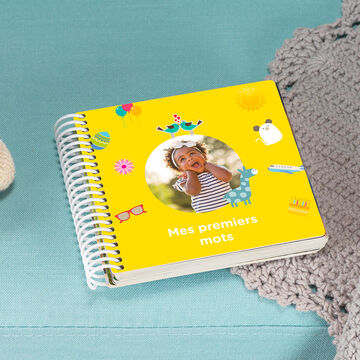 Un livre photo cartonné pour bébé fermé dont la couverture montre une image d'un enfant et écrit dessus "Mes premiers mots"