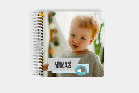 Un livre photo cartonné pour bébé fermé dont la couverture montre une image d'un enfant et écrit dessus "Nikas"