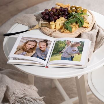 Un mini album photo carré 15x15 cm ouvert et posé sur la table avec une couverture affichant des amies