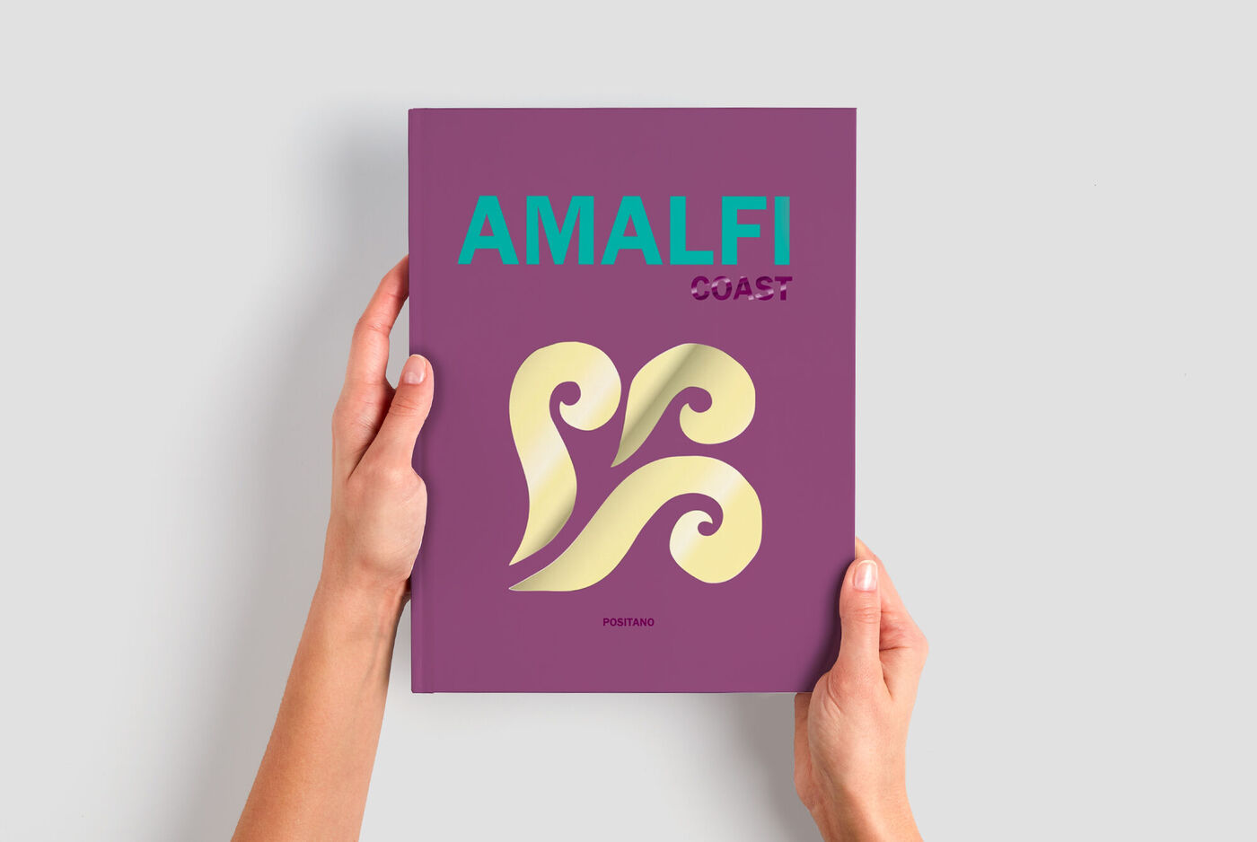 Livre photo personnalisé CEWE violet, présenté en main, couverture Amalfi Coast avec effet relief doré