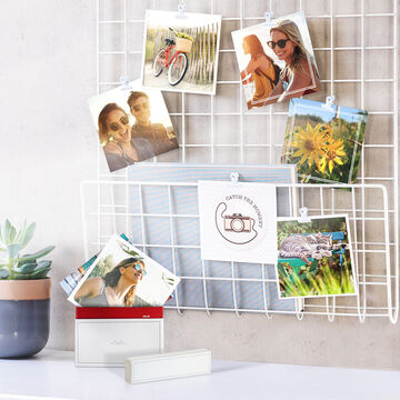 Tirages photo carré avec des souvenirs de vacances en famille, accrochés sur un panneau et dans leur boîte