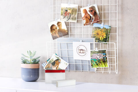 Tirages photo carré avec des souvenirs de vacances en famille, accrochés sur un panneau et dans leur boîte